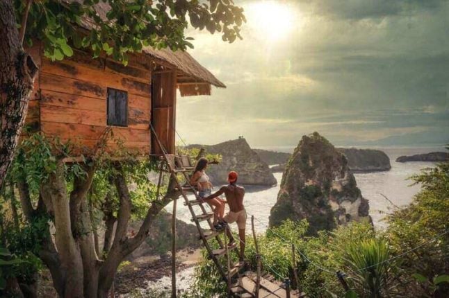 young couple posing outside treehouse overlooking ocean