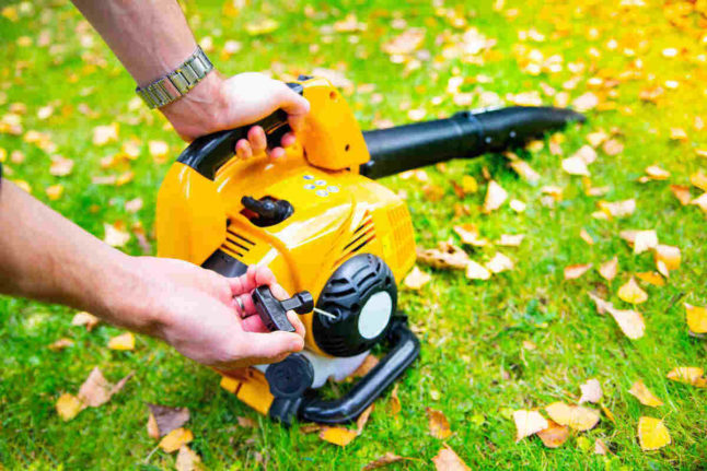 A man uses a yellow leaf vacuum to remove leaves from his yard.