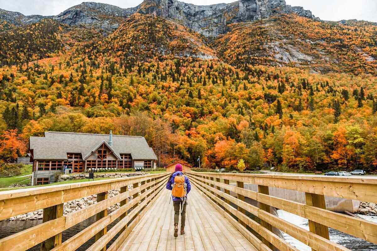 Backpacker walking over a bridge, approaching a farm in a valley against a background of hills covered in colorful fall foliage