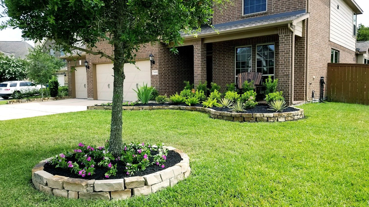 Front yard landscaped with flower bed around tree and along the front of the home.