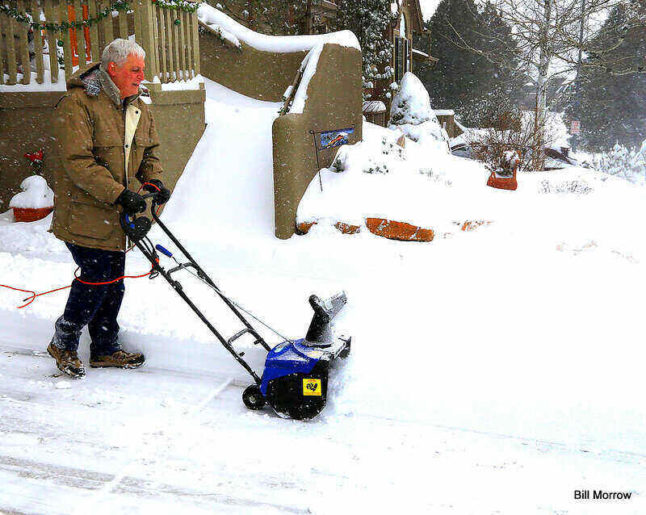 Man in winter coat pushes an electric snowblower.