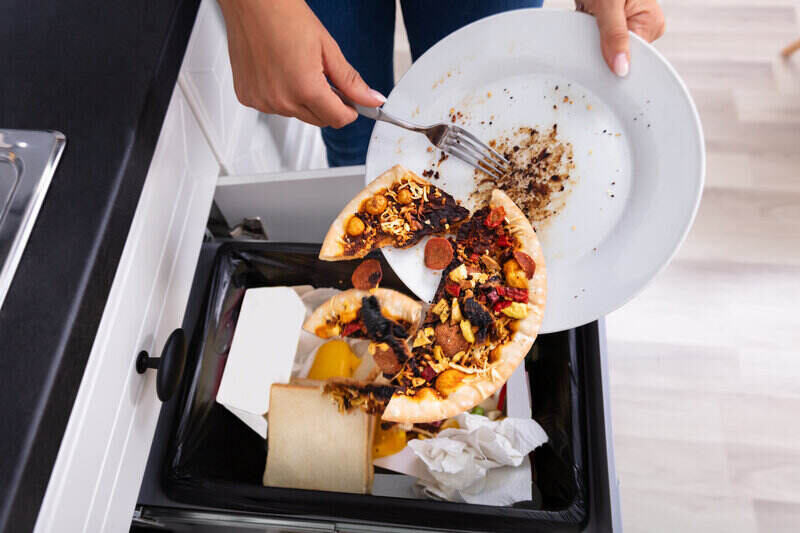 Close-up of a person throwing half of a personal-sized pizza from a plate into the trash