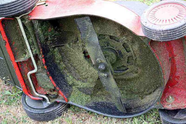 Grass caked on the underside of a lawn mower with the mower turned on its side to allow viewing of the caked-on-grass.