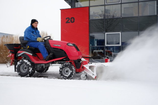 Man sits atop a red snowblower that looks more like a lawn tractor with a snowblower attachment.