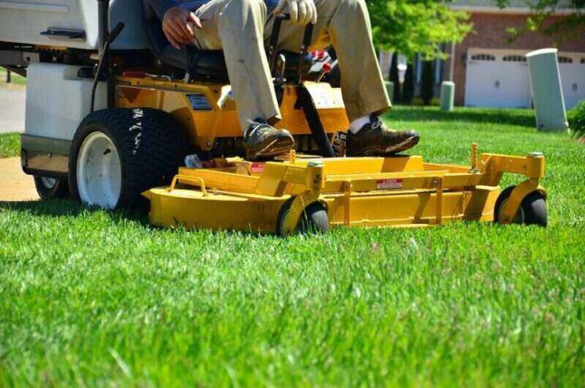 Man sitting atop a yellow zero-turn lawn mower