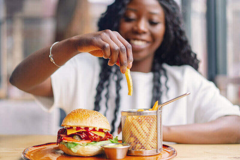 Young woman smiling and holding a fry, with a burger and fries in front of her.