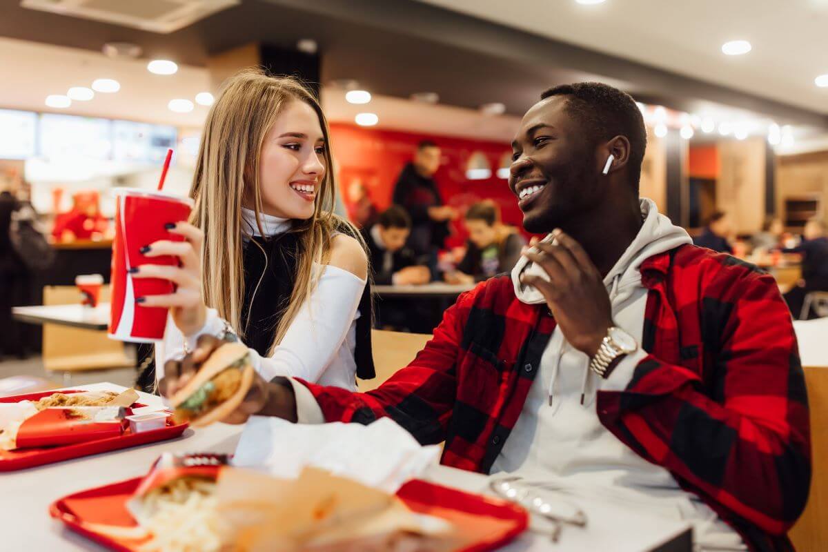 A smiling young woman and man enjoy combo meals at a fast food restaurant