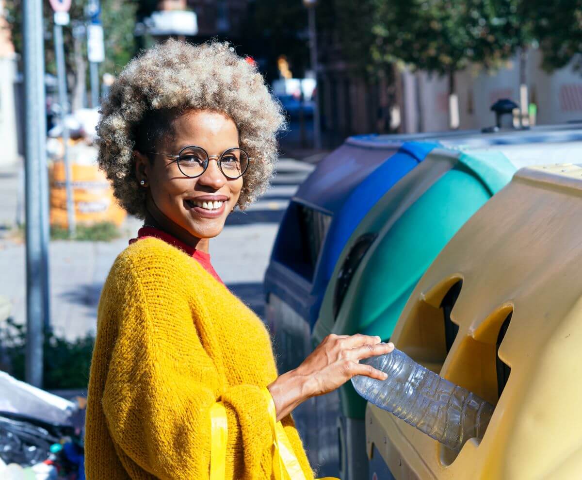 Woman throws plastic bottle into public recycling bin on street