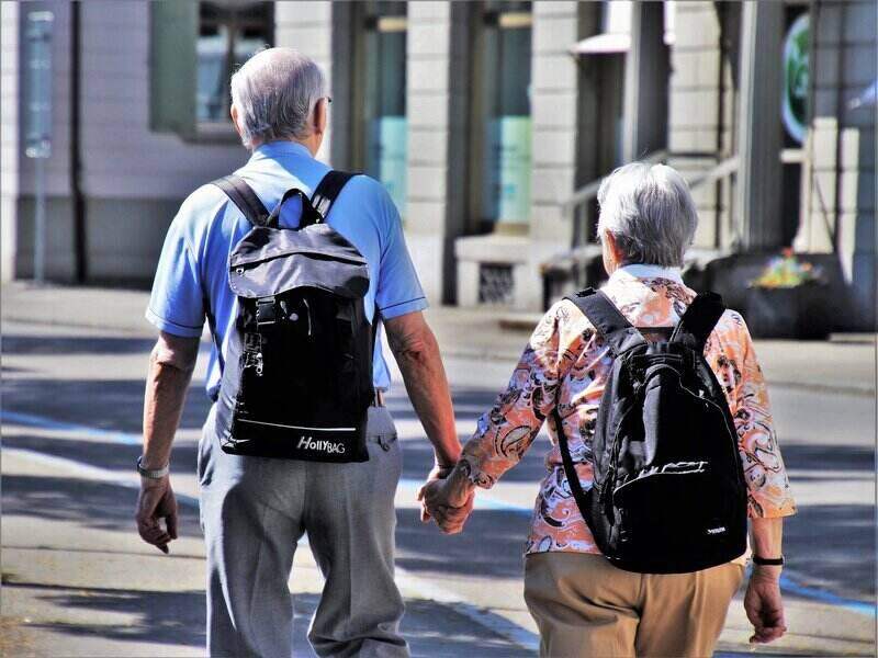 Senior couple holding hands and walking while wearing backpacks