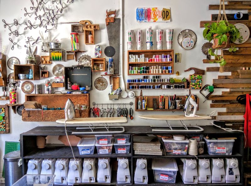 A display wall showcases an artfully curated collection of craft supplies, such as spools of thread, crayons, and sewing machines, inside the WorkshopSF space in San Francisco.