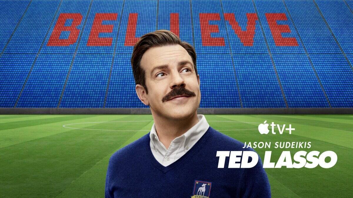 Ted Lasso (Jason Sudekis) promo photo of him standing with a soccer field and stadium in the background.