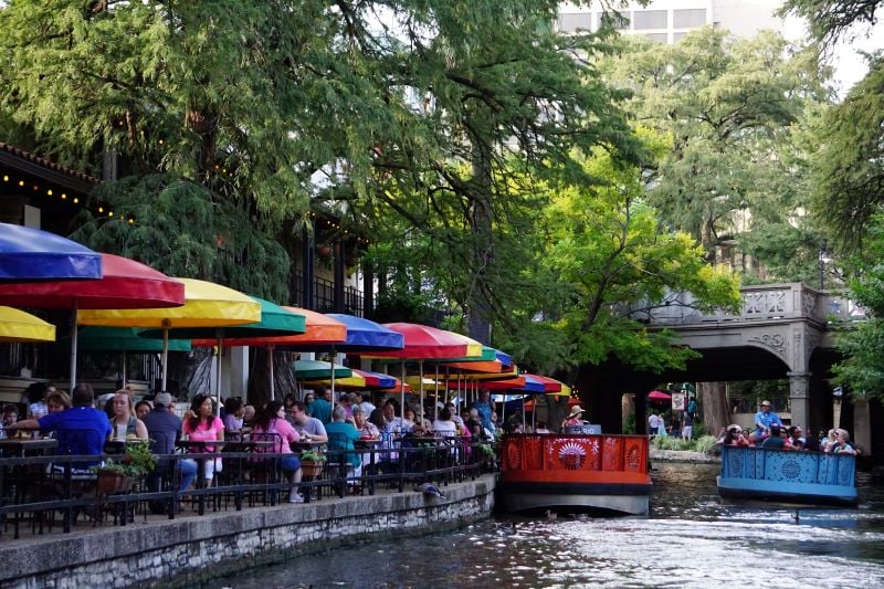 Patrons enjoy a meal under colorful umbrellas at the San Antonio Riverwalk’s Casa Rio restaurant as well as a view of boats riding along the river