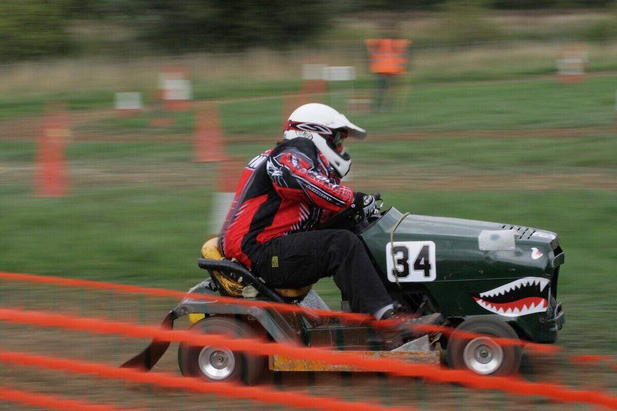 A competitor of lawn mower racing on a track with a lawn mower that has a painted mouth with teeth on the front