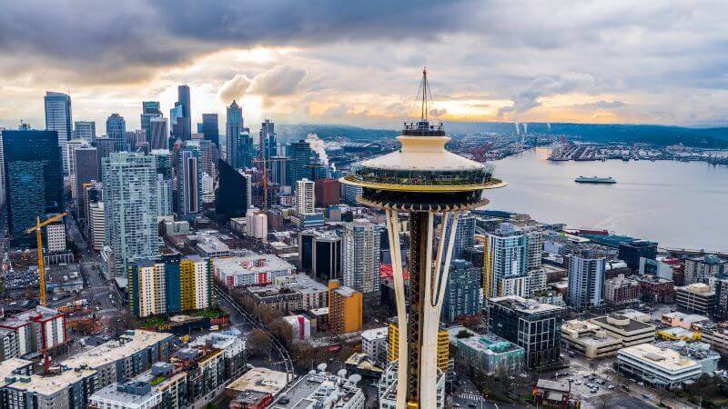 The Space Needle stands over the skyscrapers and landscape on an overcast day in Seattle.