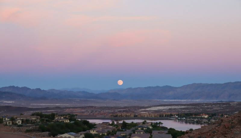 A full moon rises at sunset above mountains surrounding a residential area in Lake Las Vegas in Henderson, Nevada.