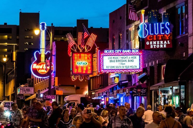 Bright neon signs invite crowds into one of several blues bars on a busy street in Memphis.