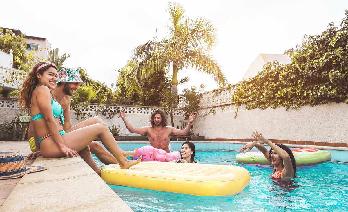 Group of young people sitting in and around a backyard pool