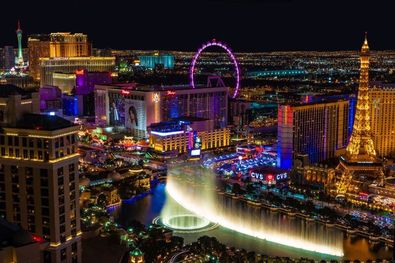A nighttime aerial view of the Las Vegas, Nevada, skyline featuring some of the most famous landmarks on The Strip, such as the Bellagio fountain, the Eiffel Tower, and the High Roller ferris wheel