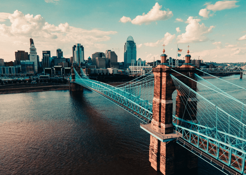 A riverfront view of Downtown Cincinnati, Ohio, with the Roebling Bridge diagonally stretching in the foreground