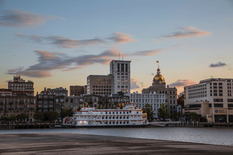 A waterfront view of the Savannah, Georgia, skyline with a docked steamboat in the center