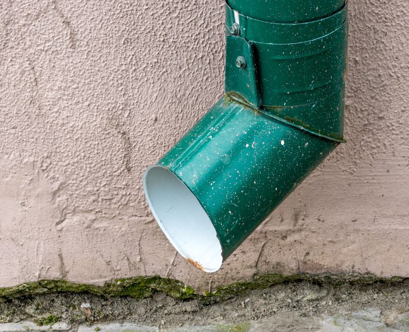 Text: Gutter Downspouts | Background Image: Green Color Gutter Downspouts