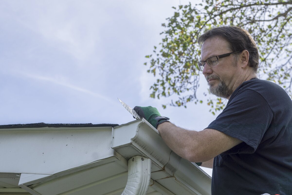Text: Pros and Cons of Gutter Guards | Background Image: Man Installing gutter Guards