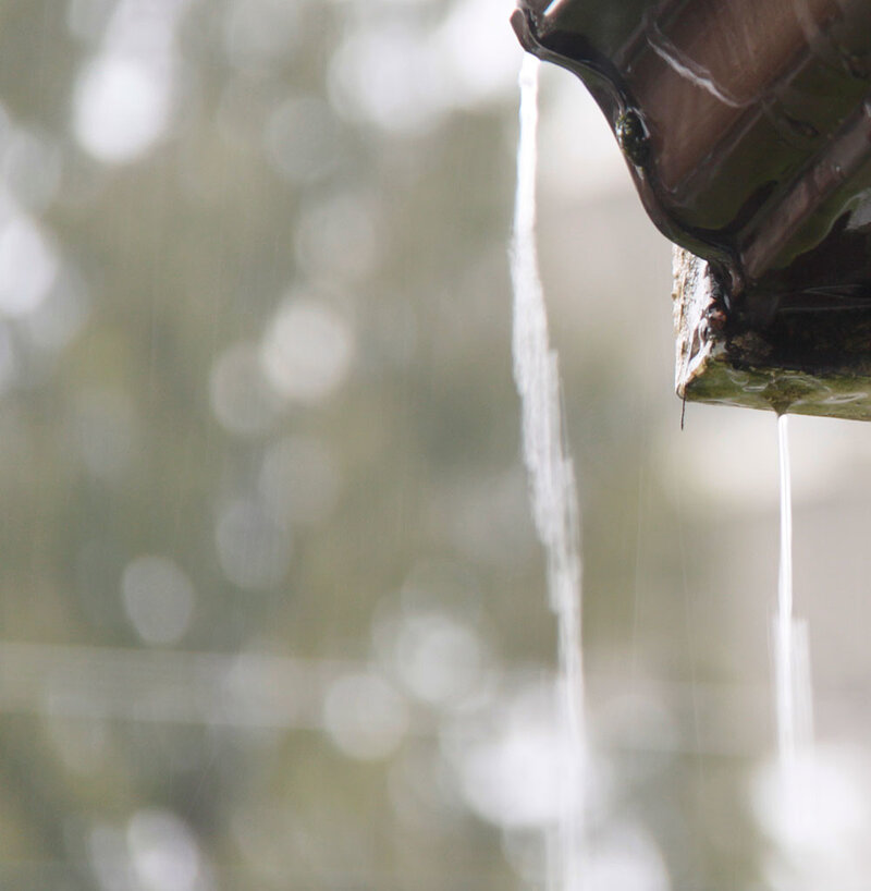 Text: Gutter Overflowing | Background Image: A gutter overflows in heavy rain