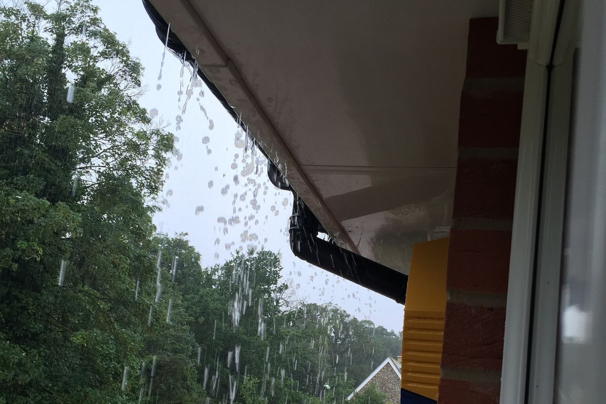 Text: Gutter Overflowing in rain | Background Image: A hour Gutter overflow in rain and water comes out