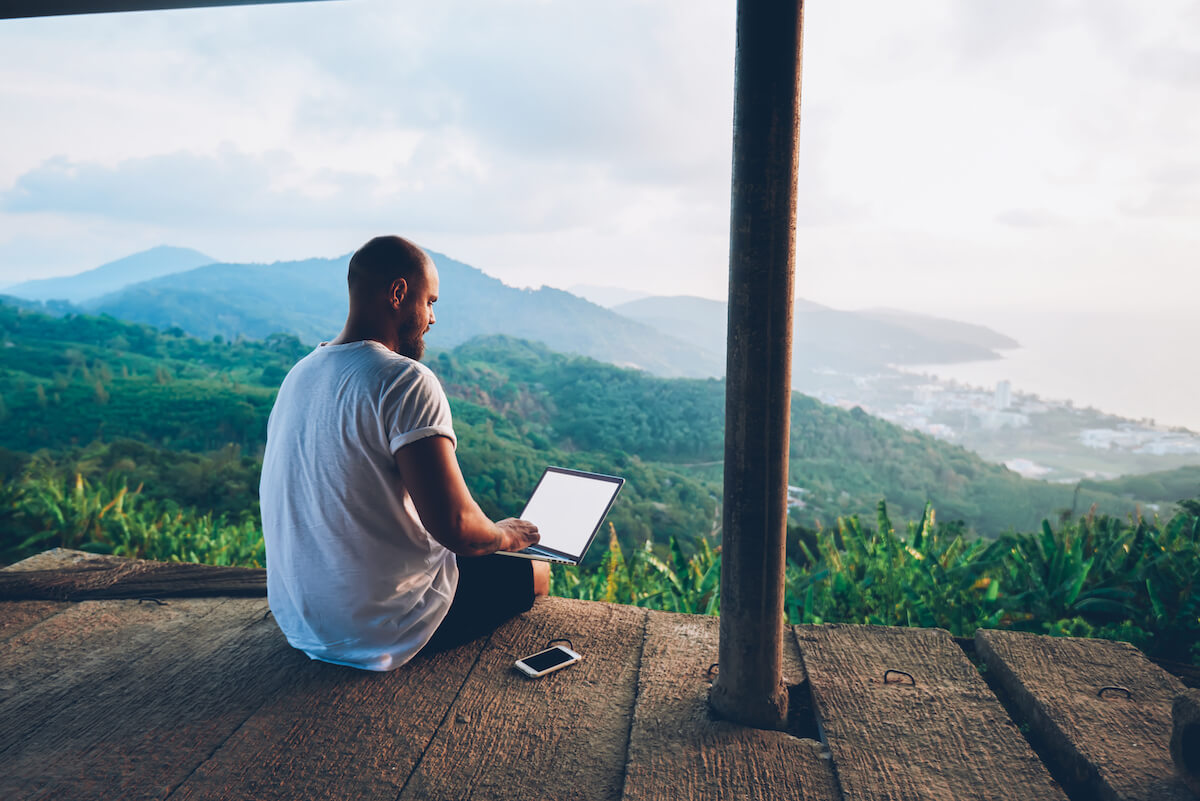Male worker using his laptop from a balcony overlooking mountains and the sea