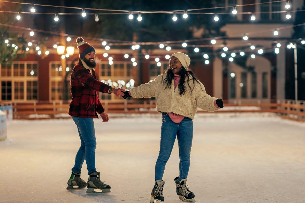 A young couple smiles while holding hands and skating around a festive ice rink
