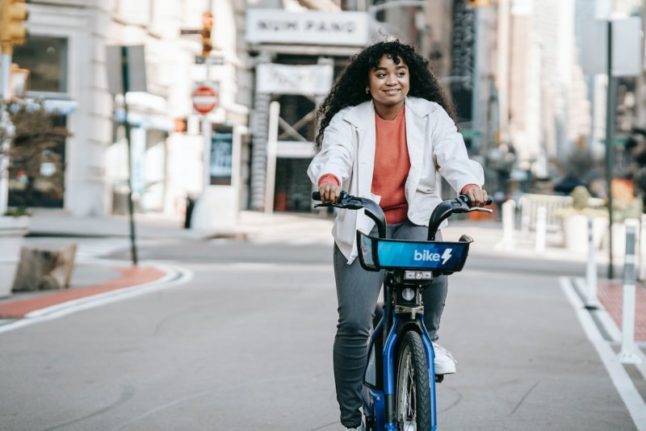 Cheerful black woman riding bicycle on street