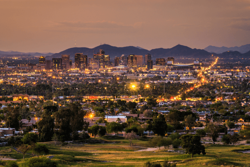 Phoenix’s skyline glitters ahead of a mountain range as the sun sets