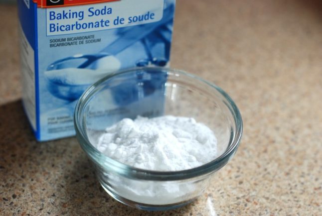 A bowl full of baking soda and a box of baking soda next to it