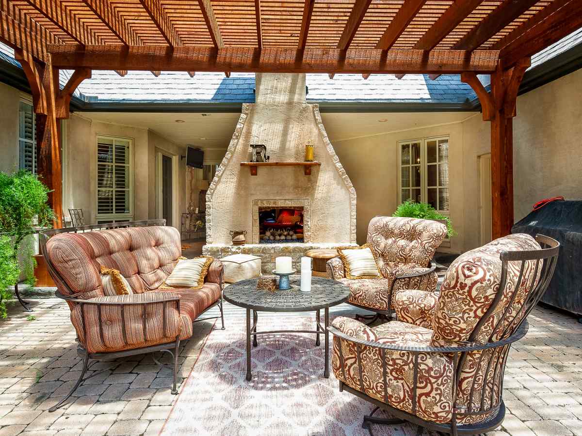 A fancy backdoor with fancy chairs and a table, a pergola and a fireplace