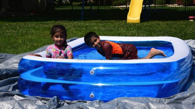 Two kids bathing in an inflatable pool laying on a tarp on the lawn