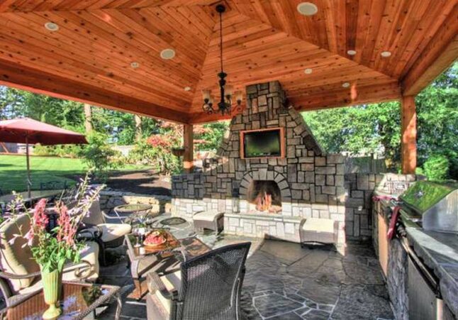 An outdoor patio with a cobblestone fireplace, table with chairs and kitchen