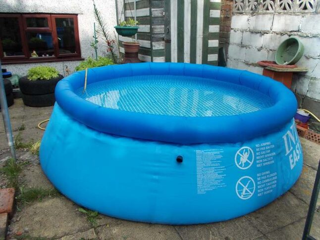 Inflatable blue pool filled with water in a backyard