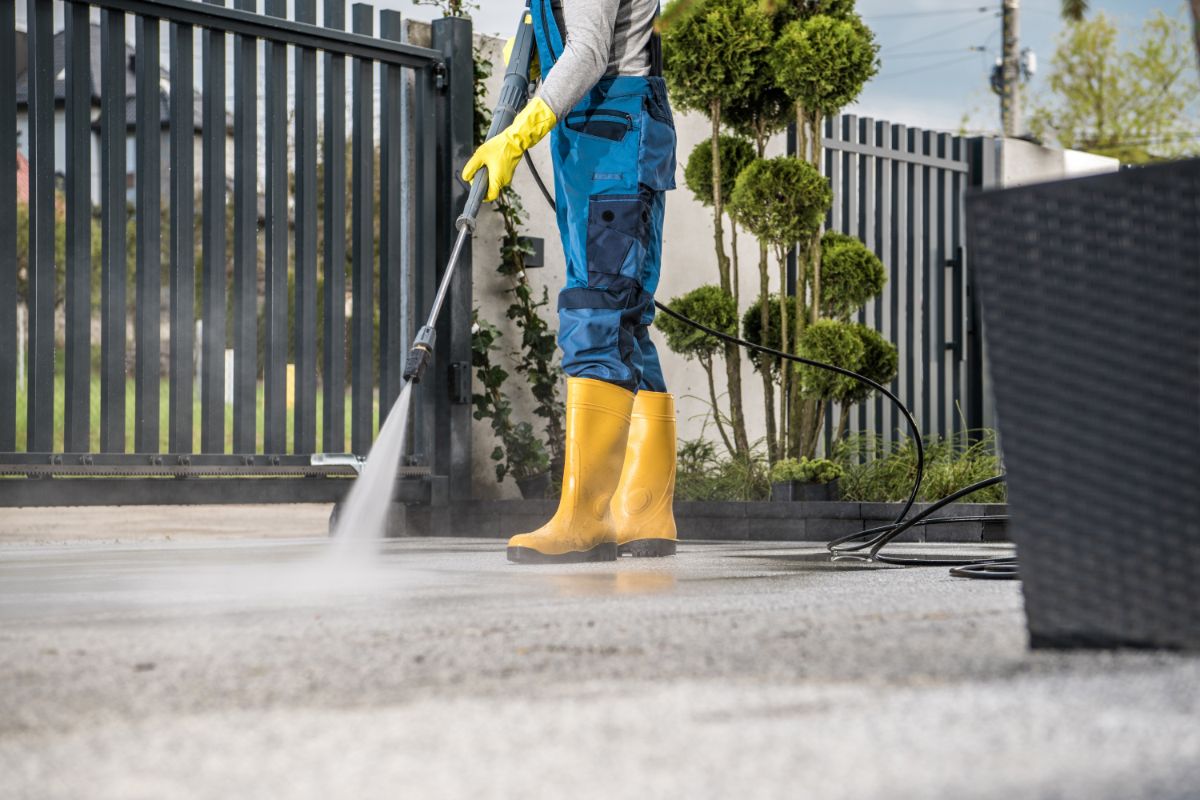 a man in yellow shoes and gloves pressure washing driveway