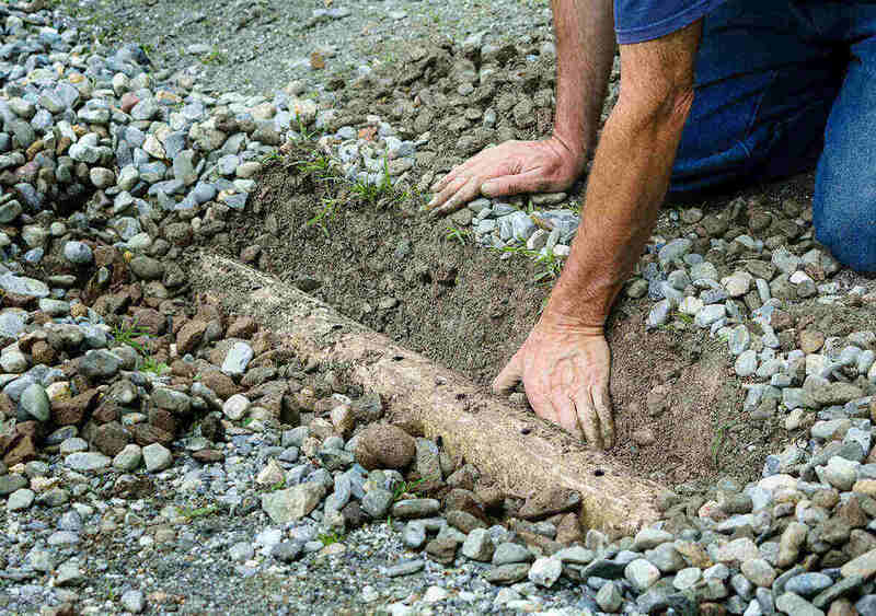 Man clears mud from drainage ditch in driveway