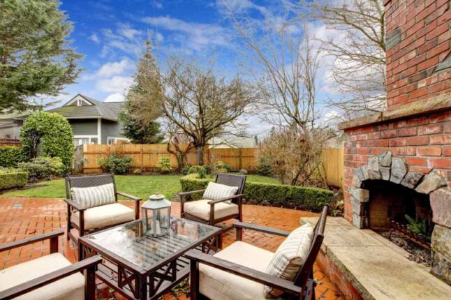 Spring fenced luxury backyard with outdoor fireplace and furniture.