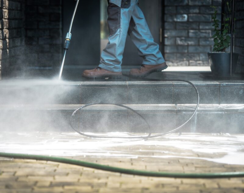 A person using pressure washer to clean the stairs and pathway