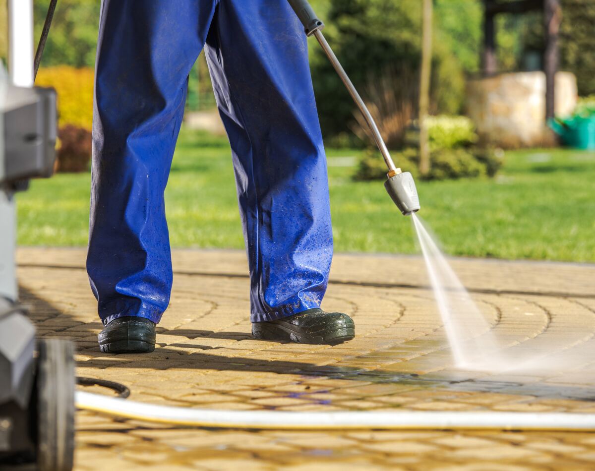 A person cleaning his concrete driveway using pressure washer