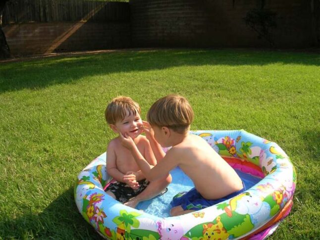 Two boys in a kiddie inflatable pool on a lawn