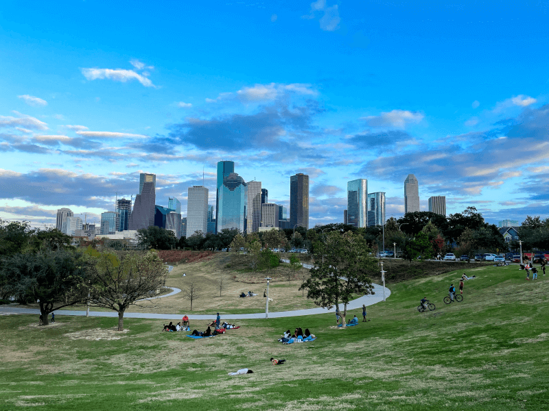 People lounge around in a park in the foreground with the Houston, Texas, skyline in the background.
