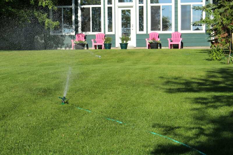 A lawn being watered with pink chairs in the background