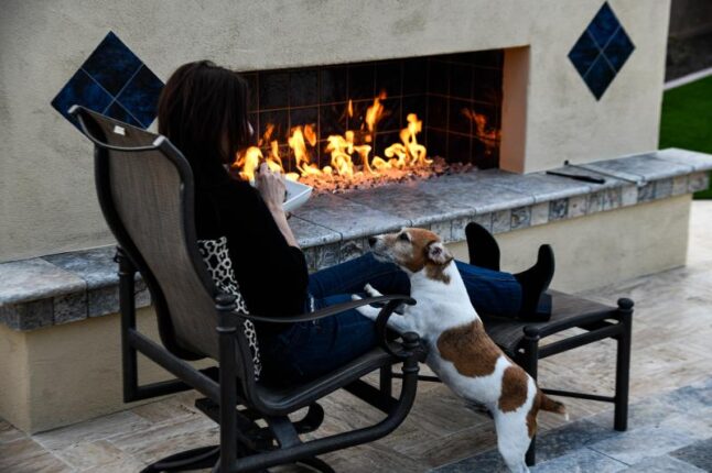 Stucco fireplace with a woman in a chair in front of it and a dog with its feet on her