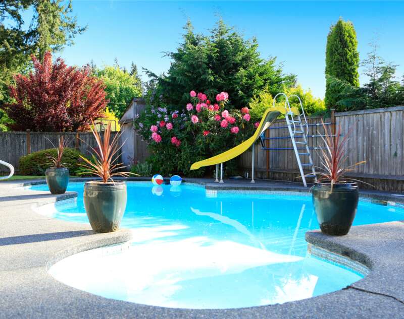 A wooden fence surrounding a pool in the backyard with a yellow slide