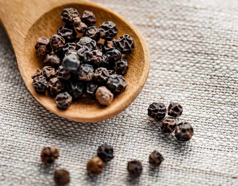 image of a black pepper in a wooden spoon
