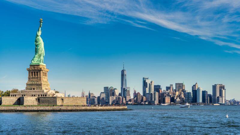 A daytime shot of the New York City skyline from the Hudson River with the Statue of Liberty in the foreground