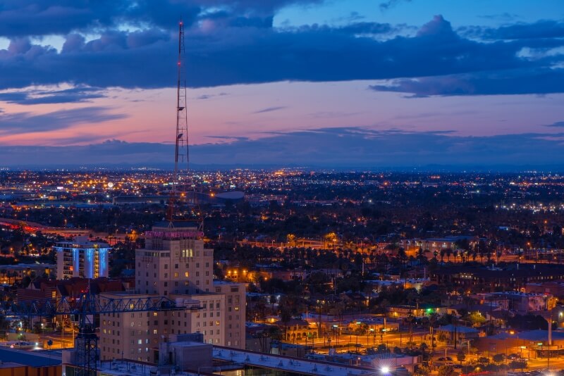 A pink sky emerges from behind dark blue clouds over the skyline of Phoenix at daybreak